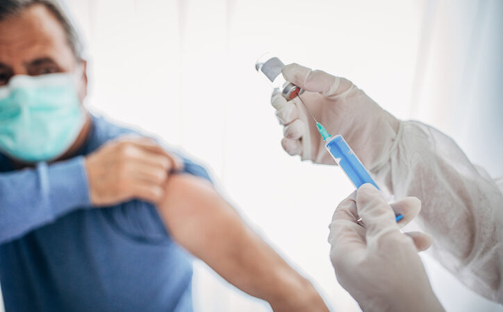 Two People, Medical Doctor In Protective Suit Giving A Senior Male Covid-19 Coronavirus Vaccine.